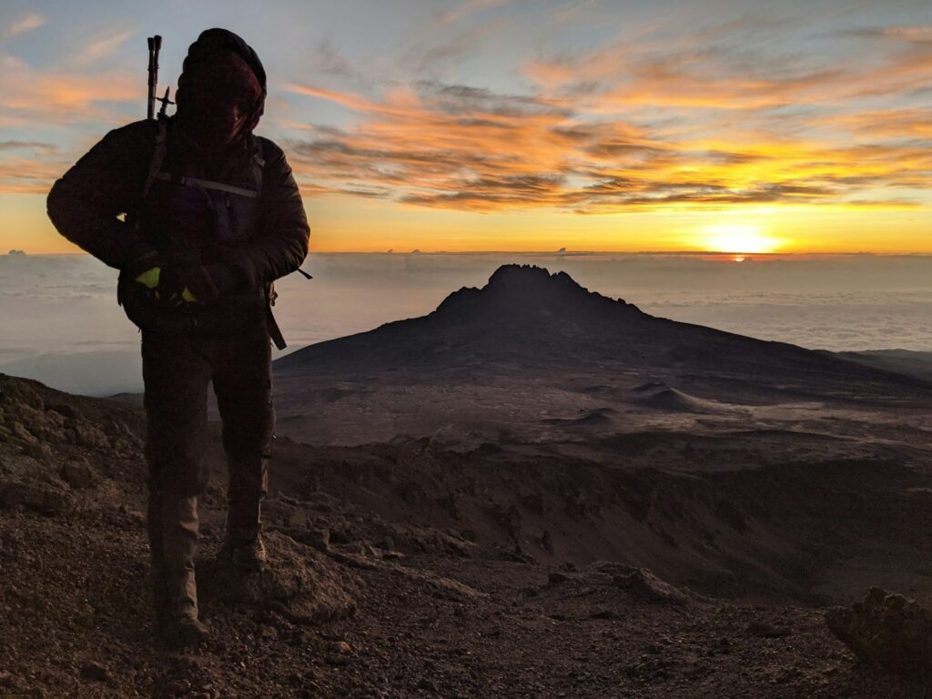 man in black jacket and pants standing on brown sand during sunset